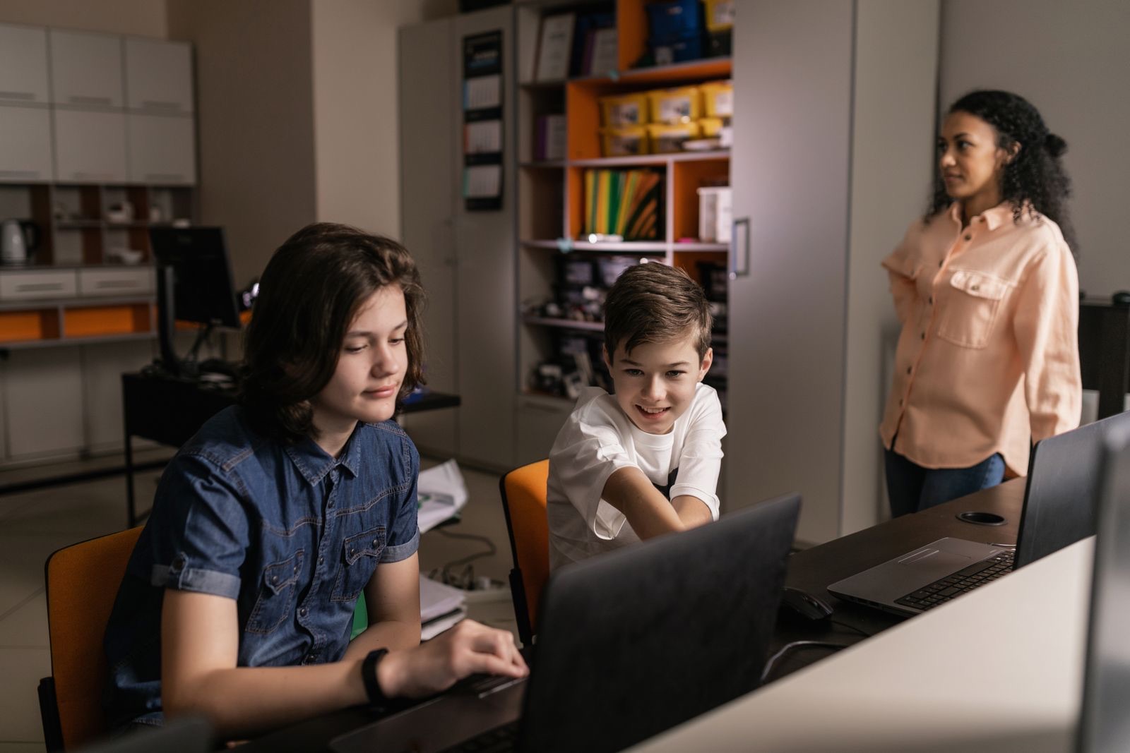 Students at laptops in a classroom, with a teacher looking on